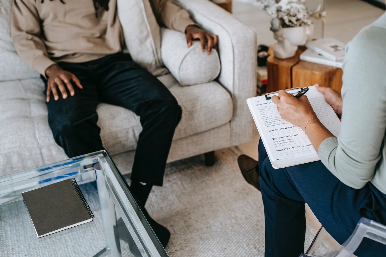 From above crop African American male in casual clothes sitting on comfy couch and answering professional female consultant questions in modern psychotherapy office